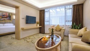 A hotel room with a bed, a sofa, a coffee table with fruit, a TV, and a large window with curtains. - Vienna Hotel (Yangshuo West Street Qianguqing Branch) (Yangshuo)