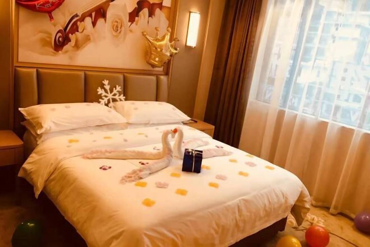 A hotel room with a bed, a nightstand, a decorative wall, and a window with curtains.