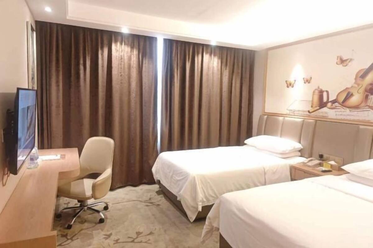 A hotel room with two beds, a desk, a chair, a TV, and a painting on the wall.