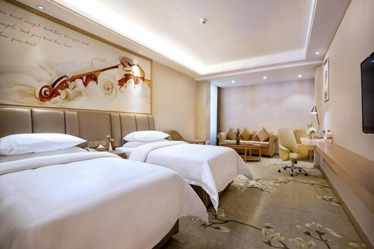 A hotel room with two beds, a sofa, a desk, and a television.