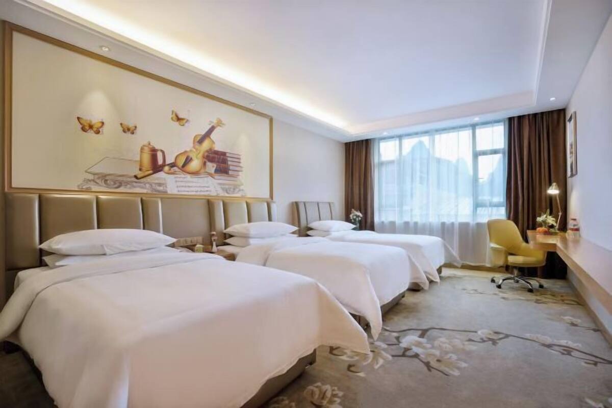 A hotel room with two beds, a desk, a chair, and a large window.