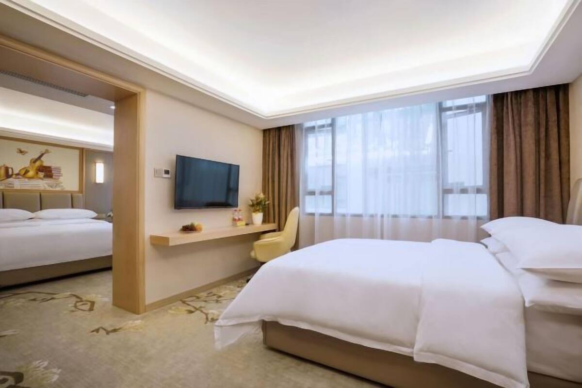 A hotel room with two beds, a TV, a desk, and a window with curtains.