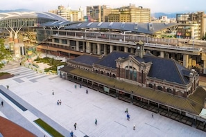 Una amplia plaza abierta con un edificio histórico, una estación de tren moderna y un puente peatonal.