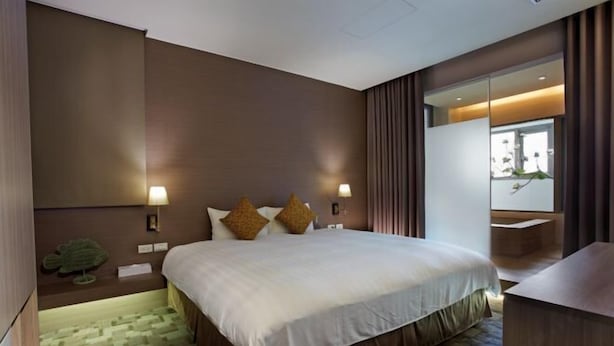 A hotel room with a large bed, two bedside lamps, a small plant, and a view of a balcony. - Micasa Hotel (Taichung)