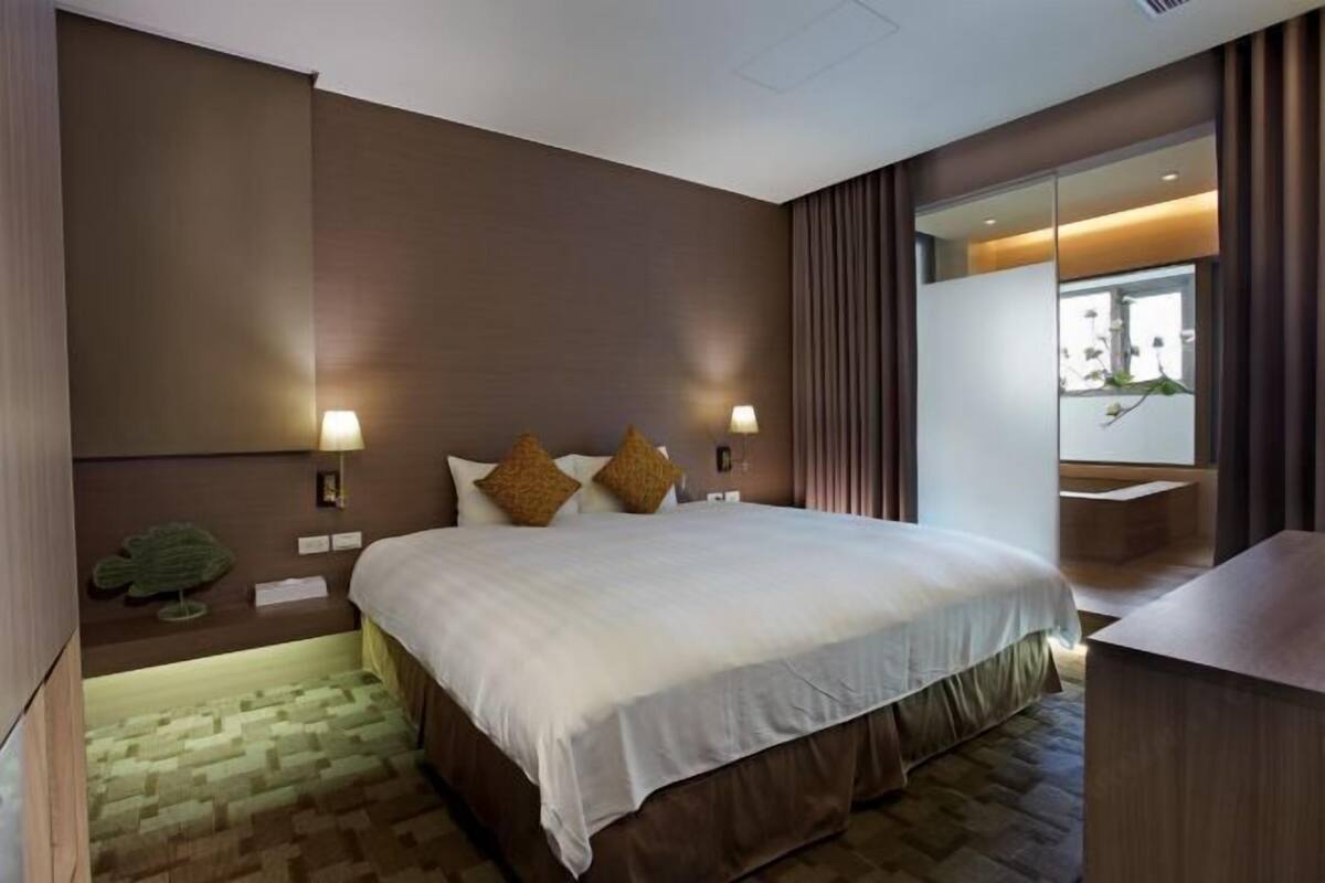 A hotel room with a large bed, two bedside lamps, a small plant, and a view of a balcony.