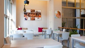 A modern cafe with white tables and chairs, a coffee-themed wall art, and large windows. - Micasa Hotel (Taichung)