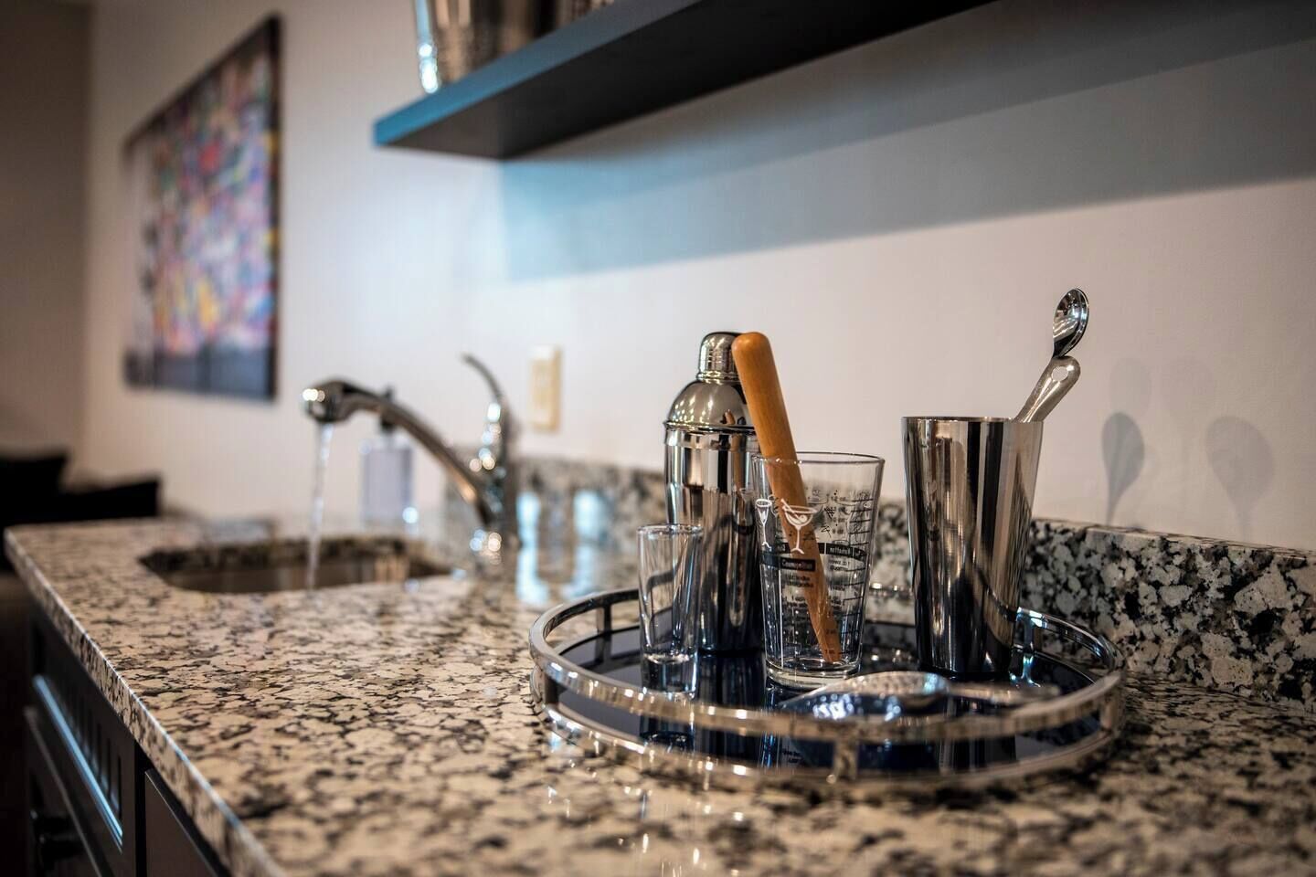 A kitchen counter with a granite surface, a barista station with a milk frothing pitcher, a glass, and a metal pitcher.
