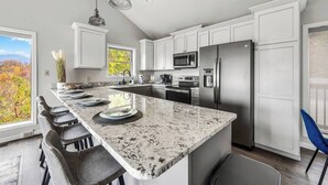 Una cocina moderna con una isla grande, electrodomésticos de acero inoxidable y vistas a las hojas otoñales.