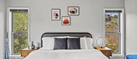 A bedroom with a large bed, two bedside tables, and three framed artworks on the wall.