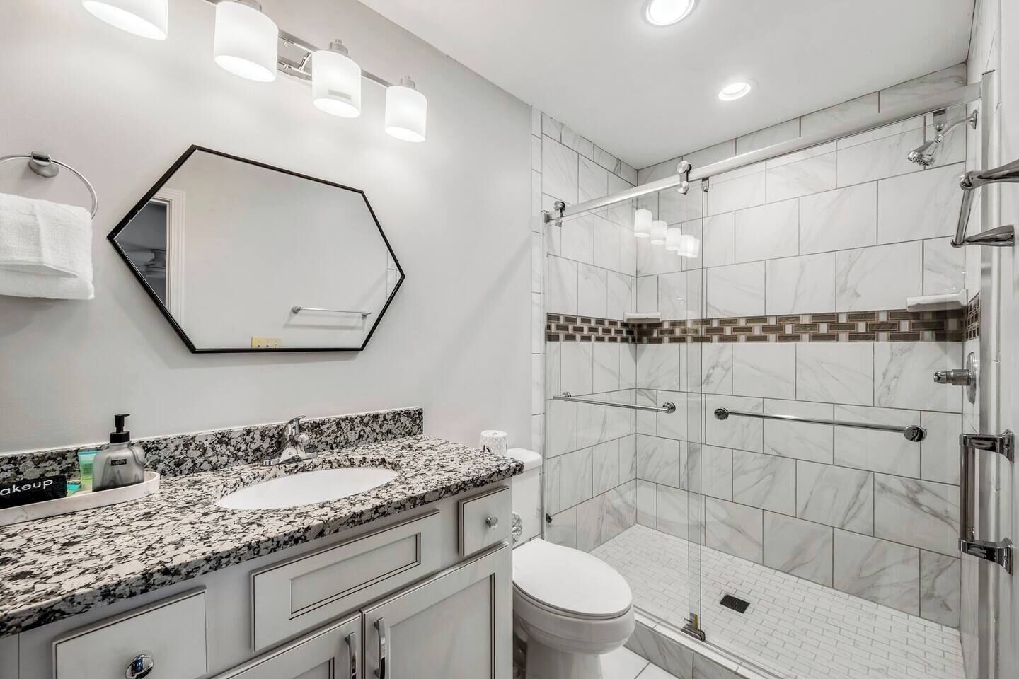 Un baño moderno con encimera de granito, un espejo grande y cabina de ducha con mampara de vidrio.