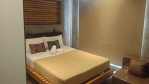 A compact hotel room with a bed, a wooden headboard, a small table, and a window. - Ramos Hello Stay Cebu (Cebu City)