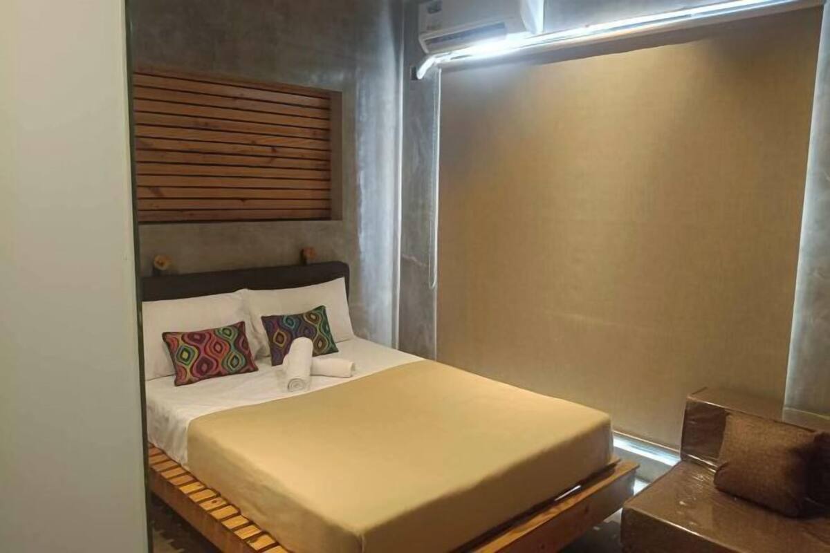 A compact hotel room with a bed, a wooden headboard, a small table, and a window.