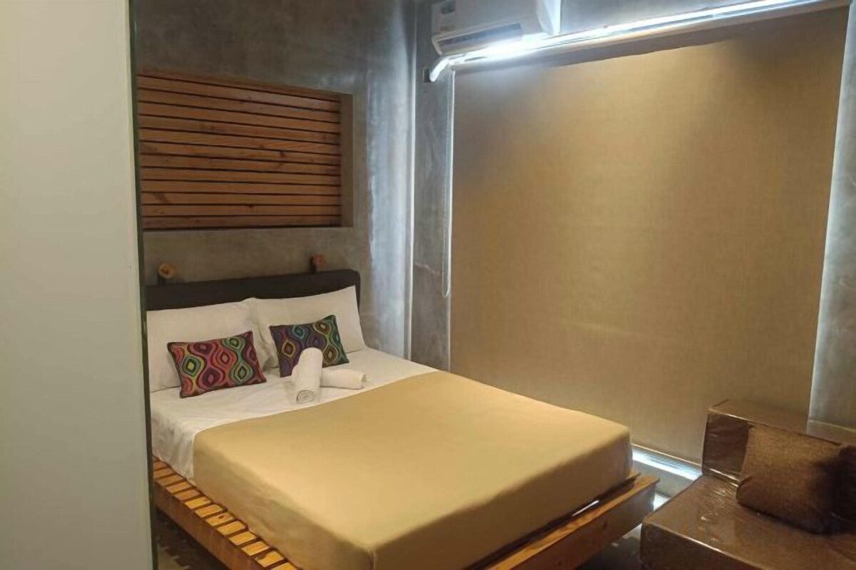 A bed with a wooden headboard, a bedside table, and a window with blinds.
