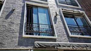 A building facade with stone-textured walls, large windows with metal railings, and a covered entrance area. - Ramos Hello Stay Cebu (Cebu City)