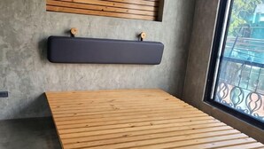 A room with a wooden slatted bed, a dark wall-mounted shelf, and a window with a metal railing. - Ramos Hello Stay Cebu (Cebu City)