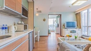 Et moderne køkken med mikrobølgeovn, elkedel og vandflasker. Der er et spiseområde med et bord og stole, samt en stue med sofa og fjernsyn.
