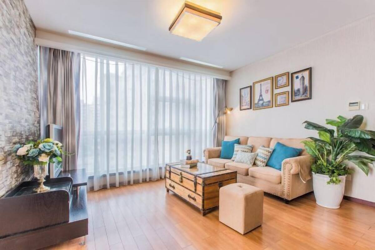 Ein Wohnzimmer mit einer Couch, einem Hocker, einem Couchtisch und einer Zimmerpflanze.