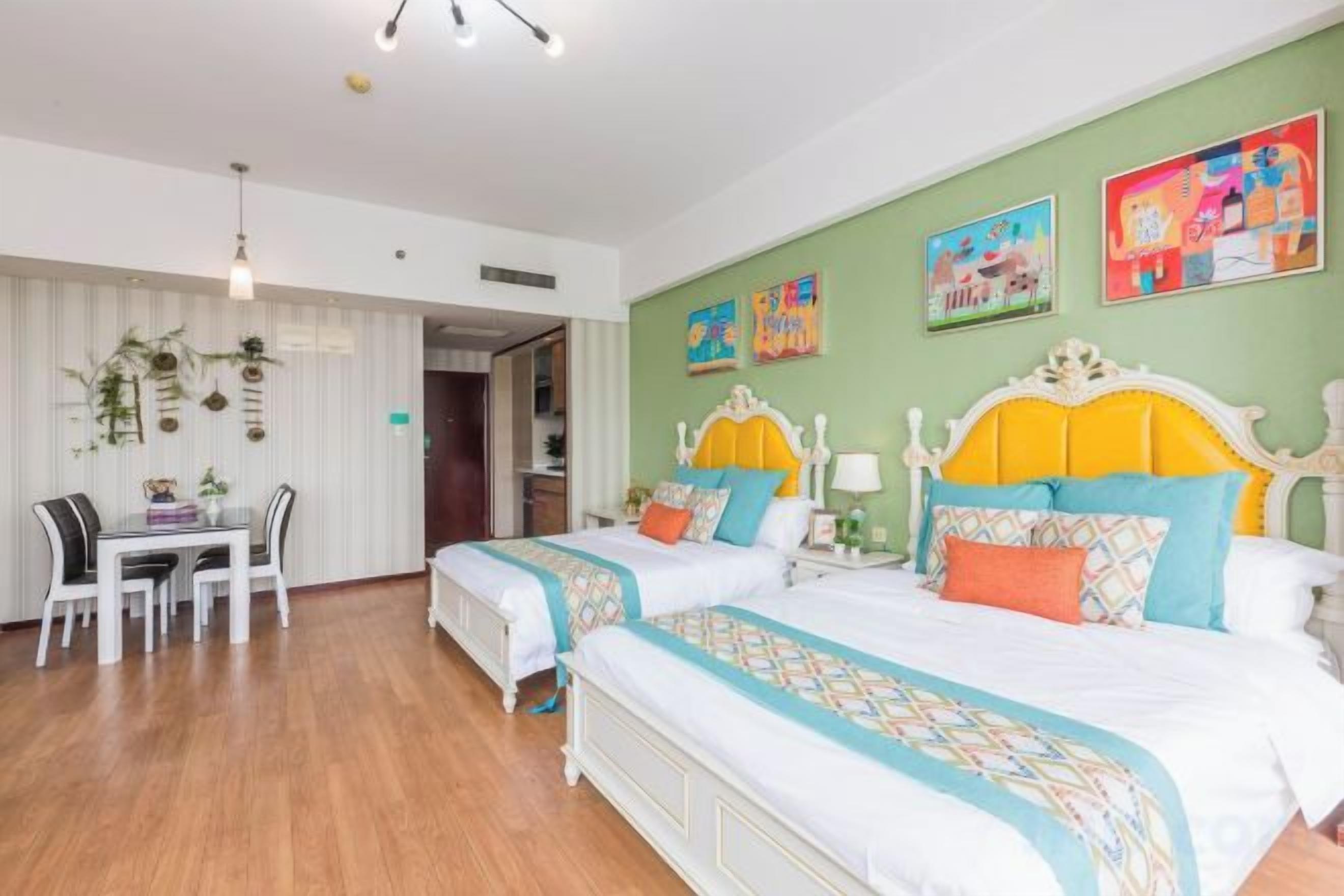 Een hotelkamer met twee bedden, een eettafel en een groene muur met kunstwerken.