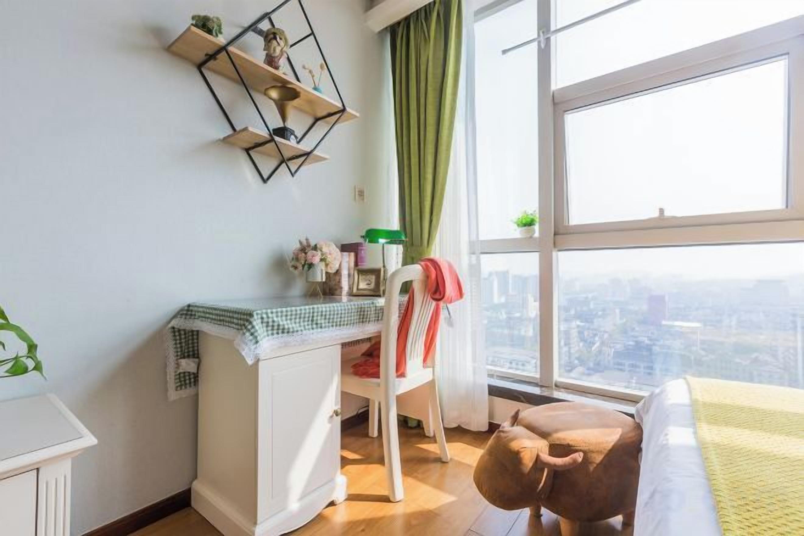A room with a desk, chair, and a view of the city through a large window.