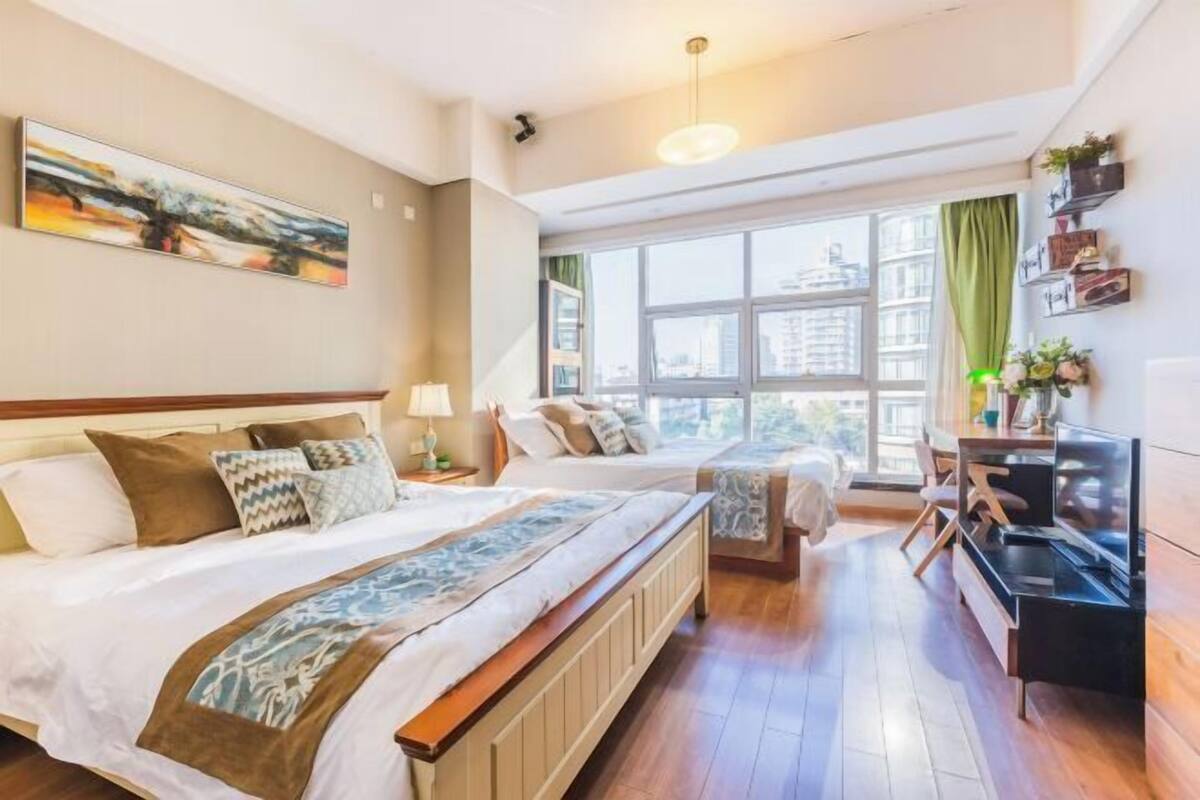 Ein Hotelzimmer mit zwei Betten, einem Fernseher, einem Schreibtisch und einem großen Fenster mit Blick auf die Stadt.