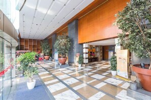 A spacious lobby with a checkered floor, potted plants, and a wooden reception desk. - Seven Apartment Hotel (Hangzhou)