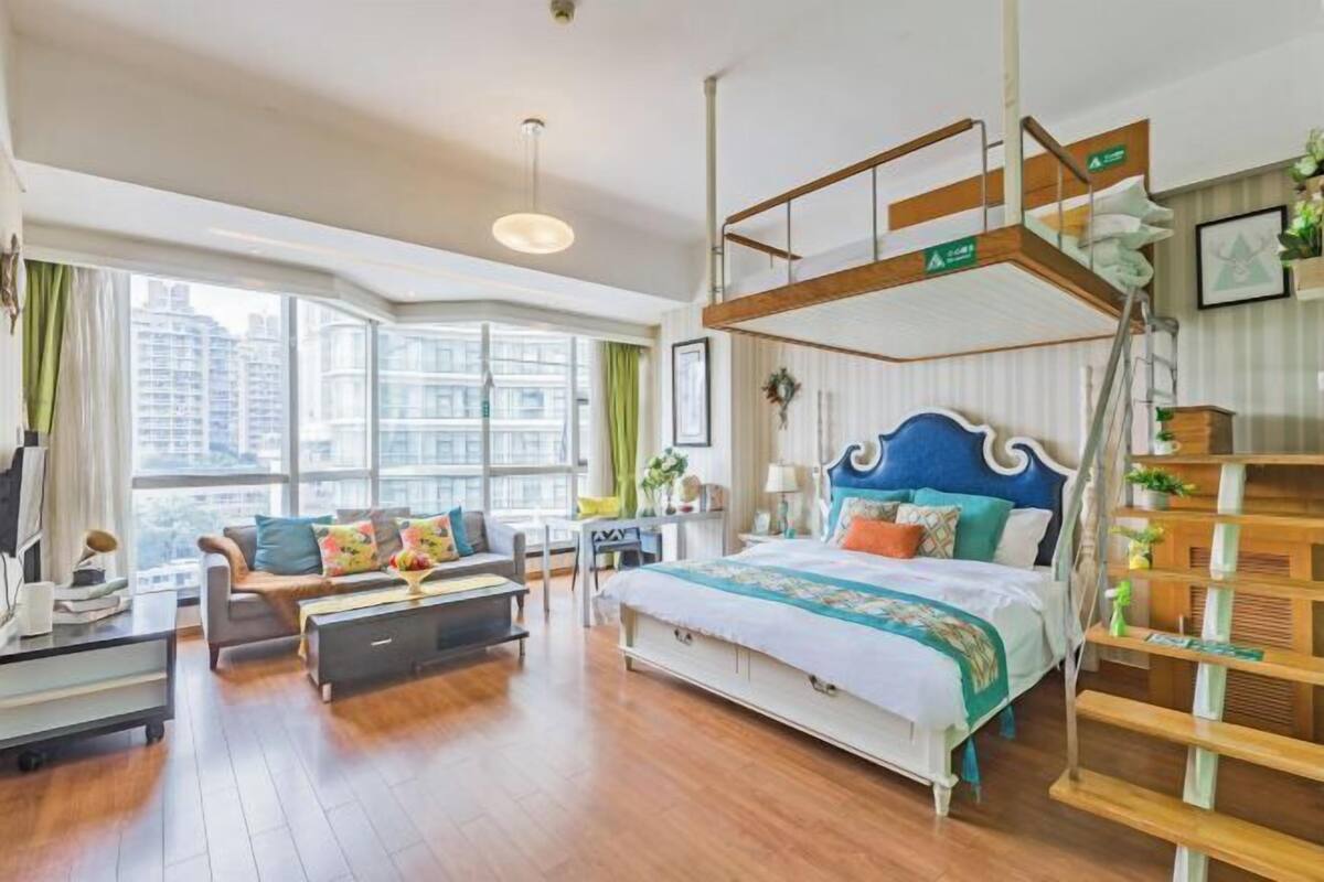 Ein modernes Hotelzimmer mit Etagenbett, einer Couch, einem Schreibtisch und großen Fenstern mit Blick auf die Stadt.