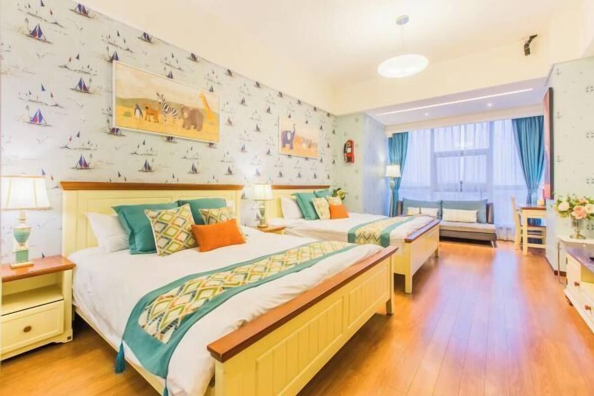 Ein Hotelzimmer mit zwei Betten, Holzboden, einem großen Fenster mit Vorhängen und einer Wand mit Meeresmotiv-Tapete.
