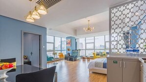 Et moderne hotelværelse med en stor seng, et spiseområde med bord og stole, et tekøkken og store vinduer med udsigt over byen.