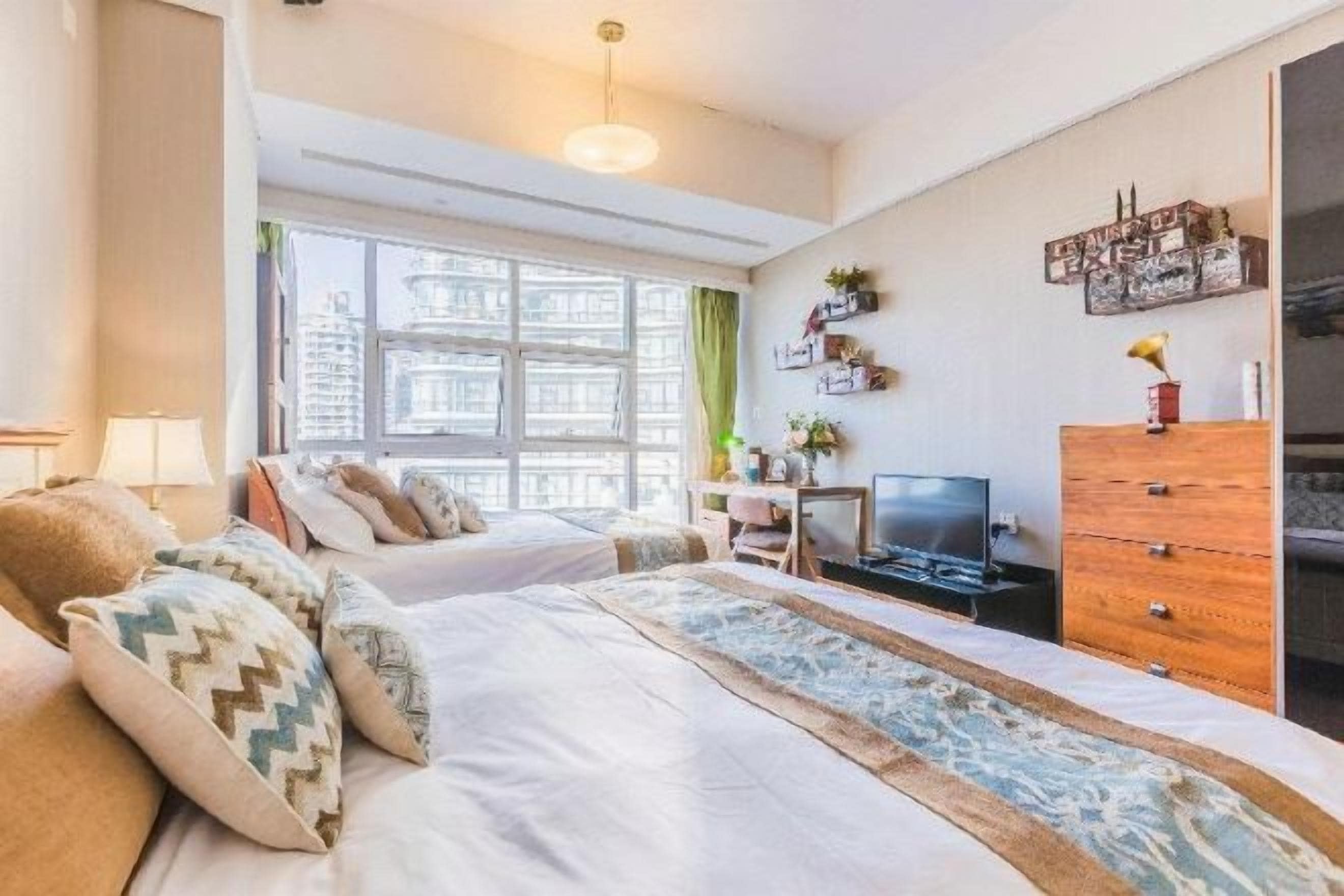 Un dormitorio con cama, cómoda, televisor y ventana.