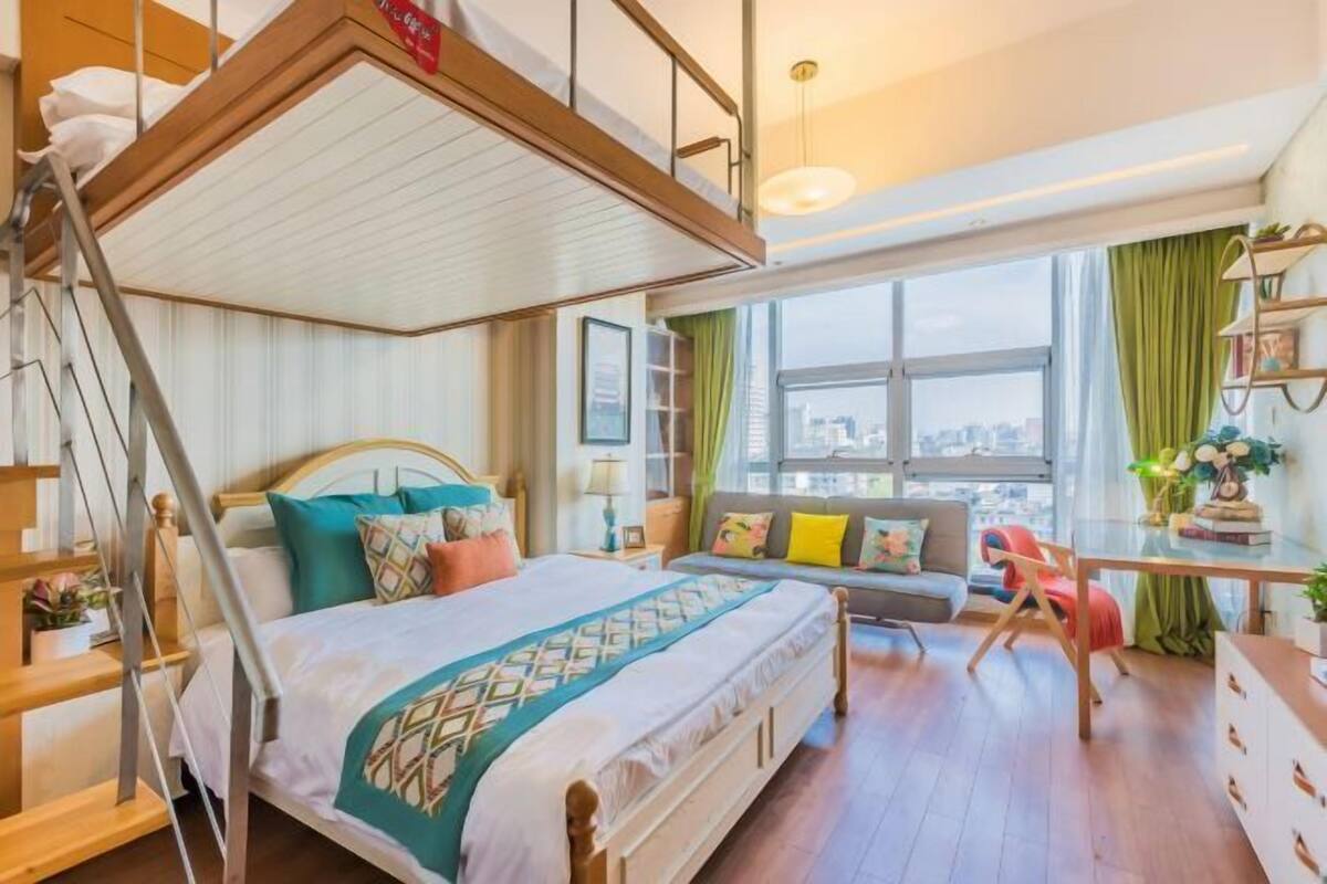 Ein Schlafzimmer mit Bett, Schreibtisch, Stuhl, Sofa und einem Fenster mit Blick auf die Stadt.