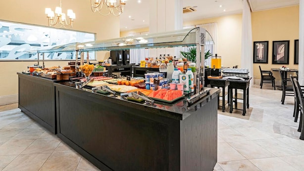 Een buffetgedeelte met diverse gerechten en drankjes, een zithoek met tafels en stoelen, en een kroonluchter.