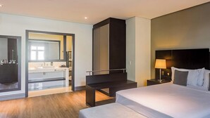 Een moderne hotelkamer met een bed, nachtkastje, lamp en uitzicht op de badkamer.