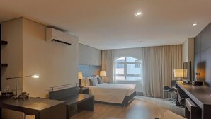 A hotel room with a bed, desk, and a large window with curtains.