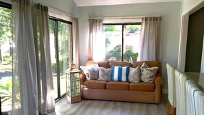 Ein Wohnzimmer mit Sofa, Tisch und Blick durch große Fenster.