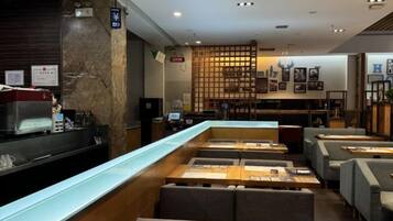 A restaurant with a long counter, seating area, and a wall with framed pictures.