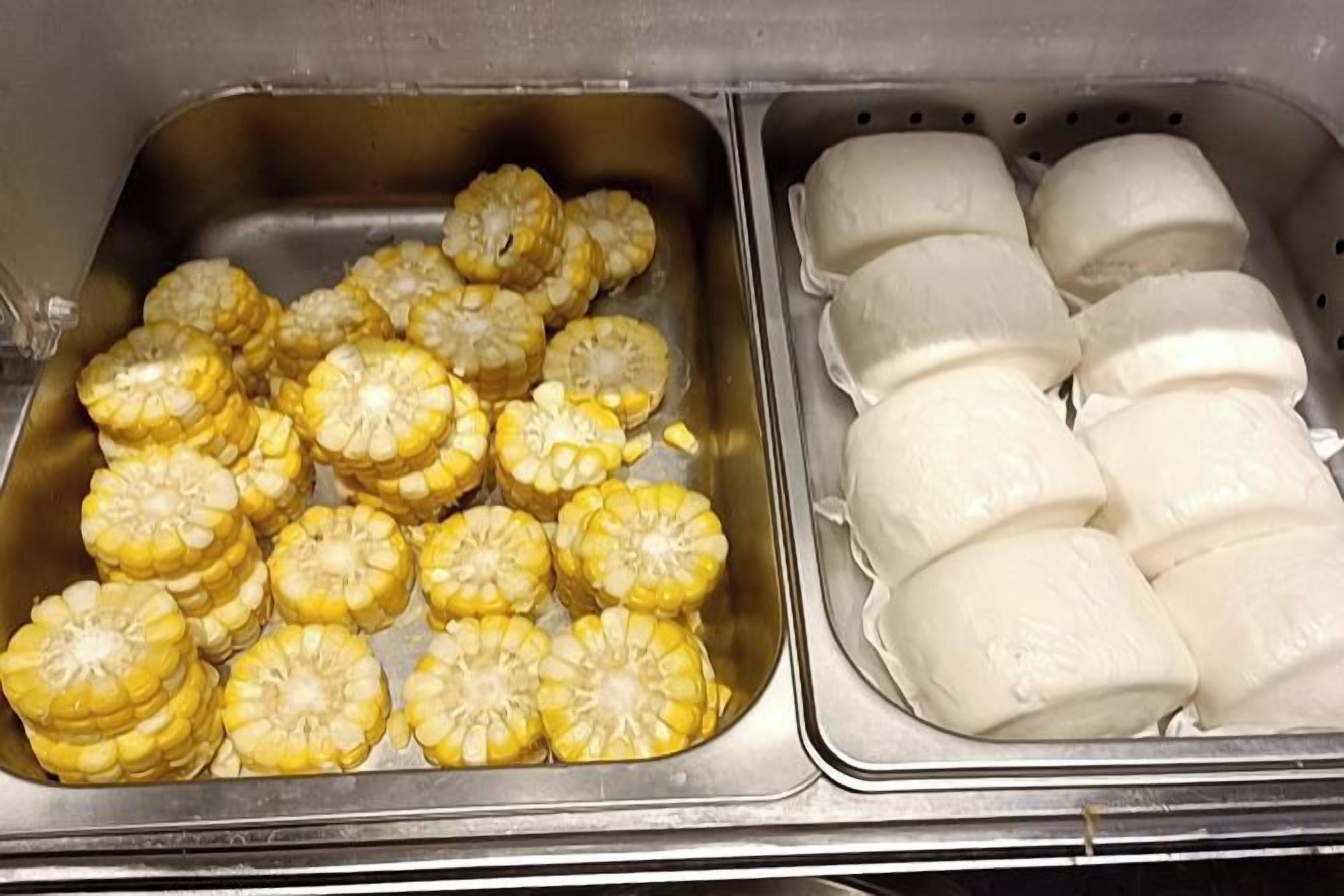 A stainless steel sink with corn on the cob and a container of white cheese.