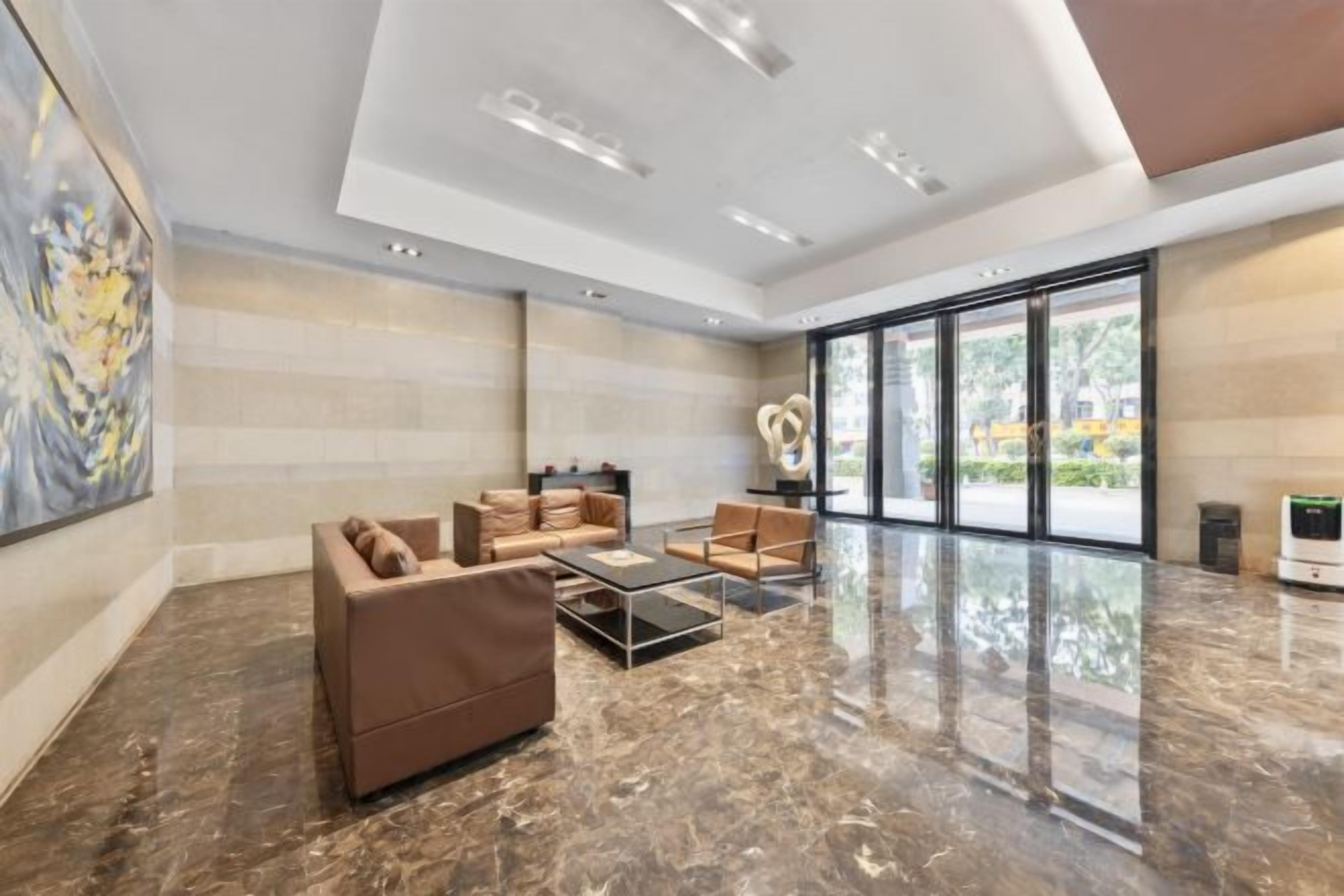 A spacious lobby with a marble floor, modern furniture, and large windows offering a view of the outdoors.