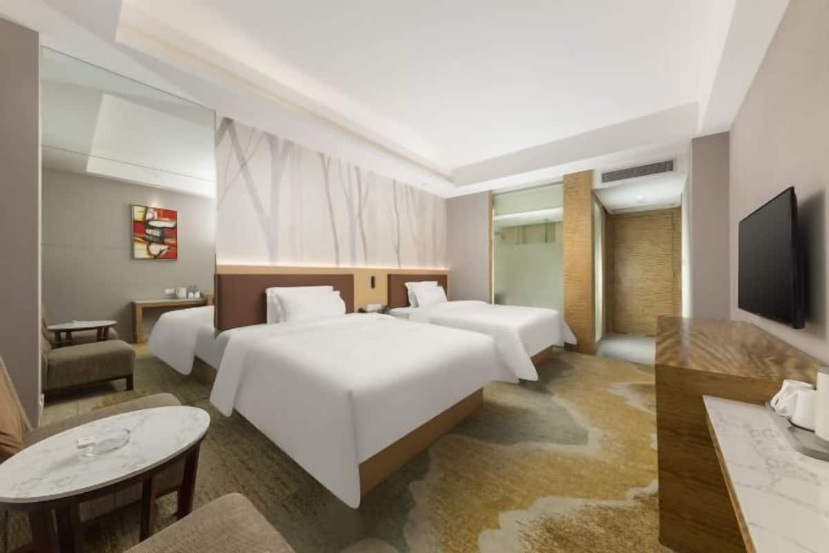 A hotel room with two beds, a small table, a chair, a TV, and a mirror.
