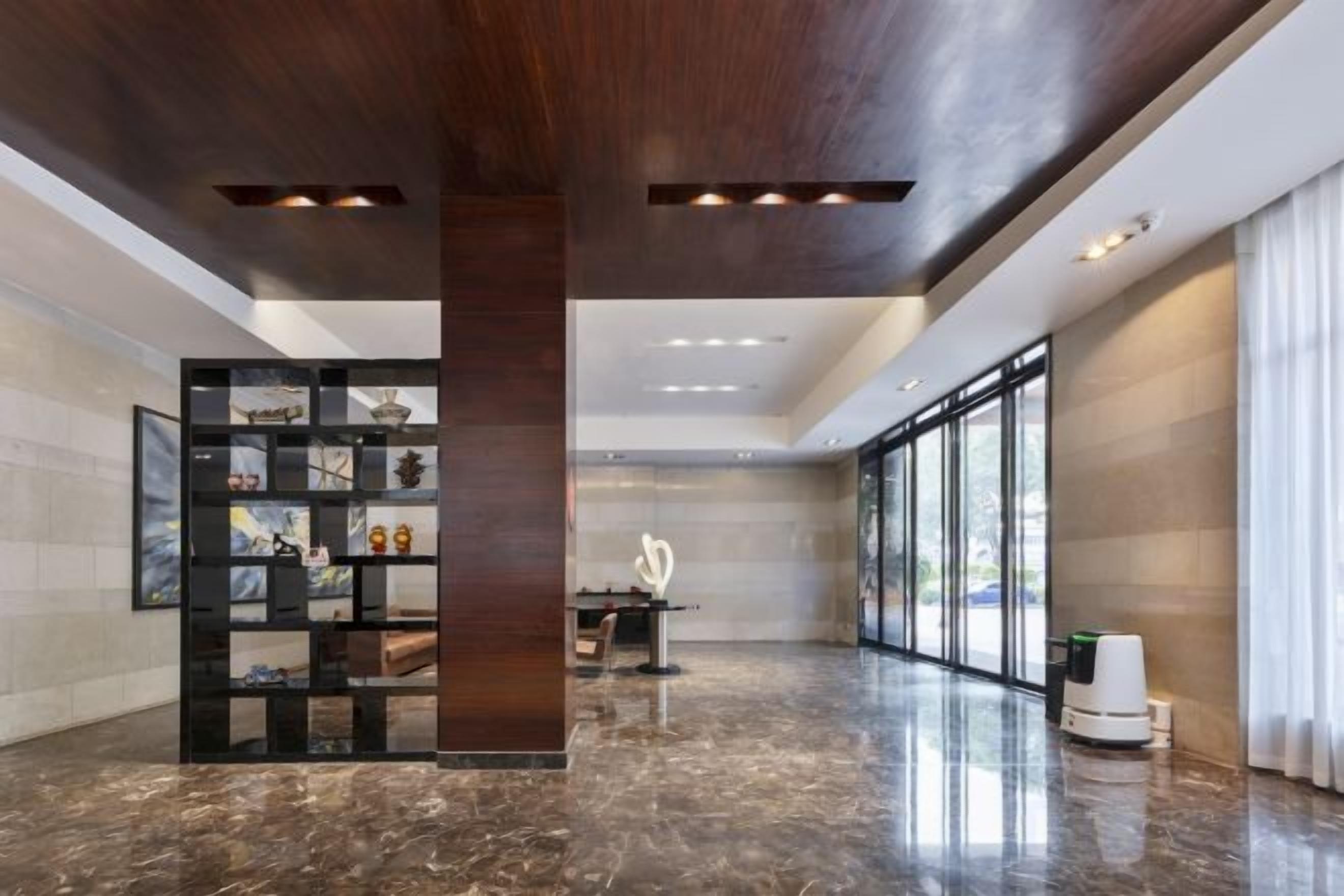 A spacious lobby with a marble floor, a central column, and a glass partition with artwork.
