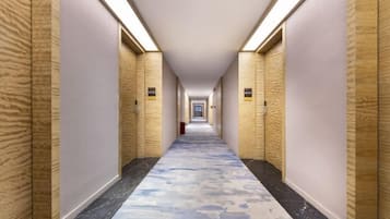 A hotel hallway with wooden paneling, a patterned carpet, and overhead lighting.