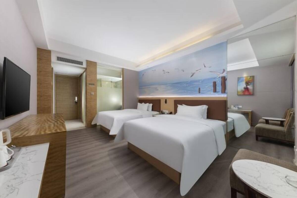 A hotel room with two beds, a TV, a desk, and a mural of birds flying over water.