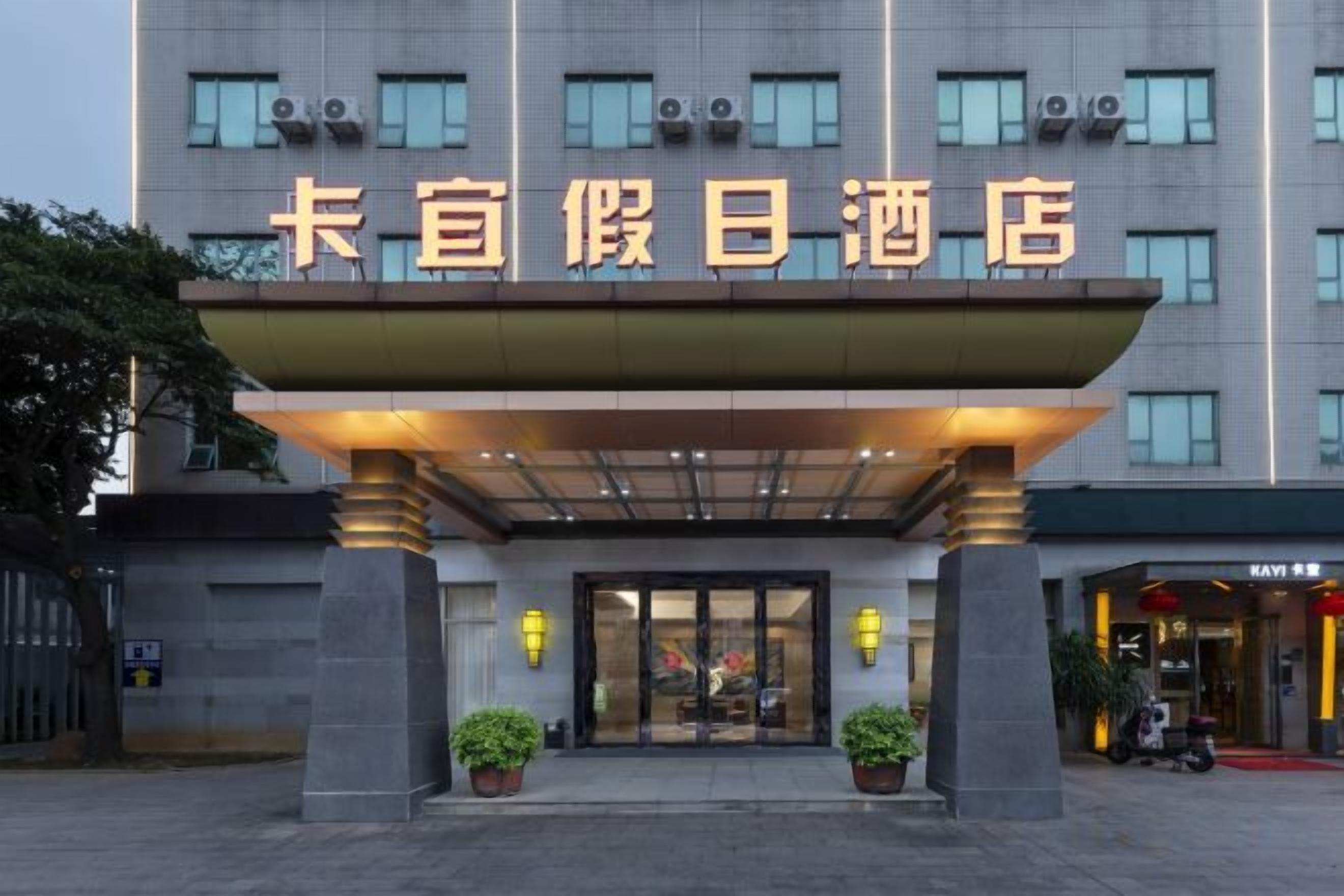 L’entrée d’un hôtel, avec une grande enseigne, un espace d’entrée abrité et des plantes en pot.
