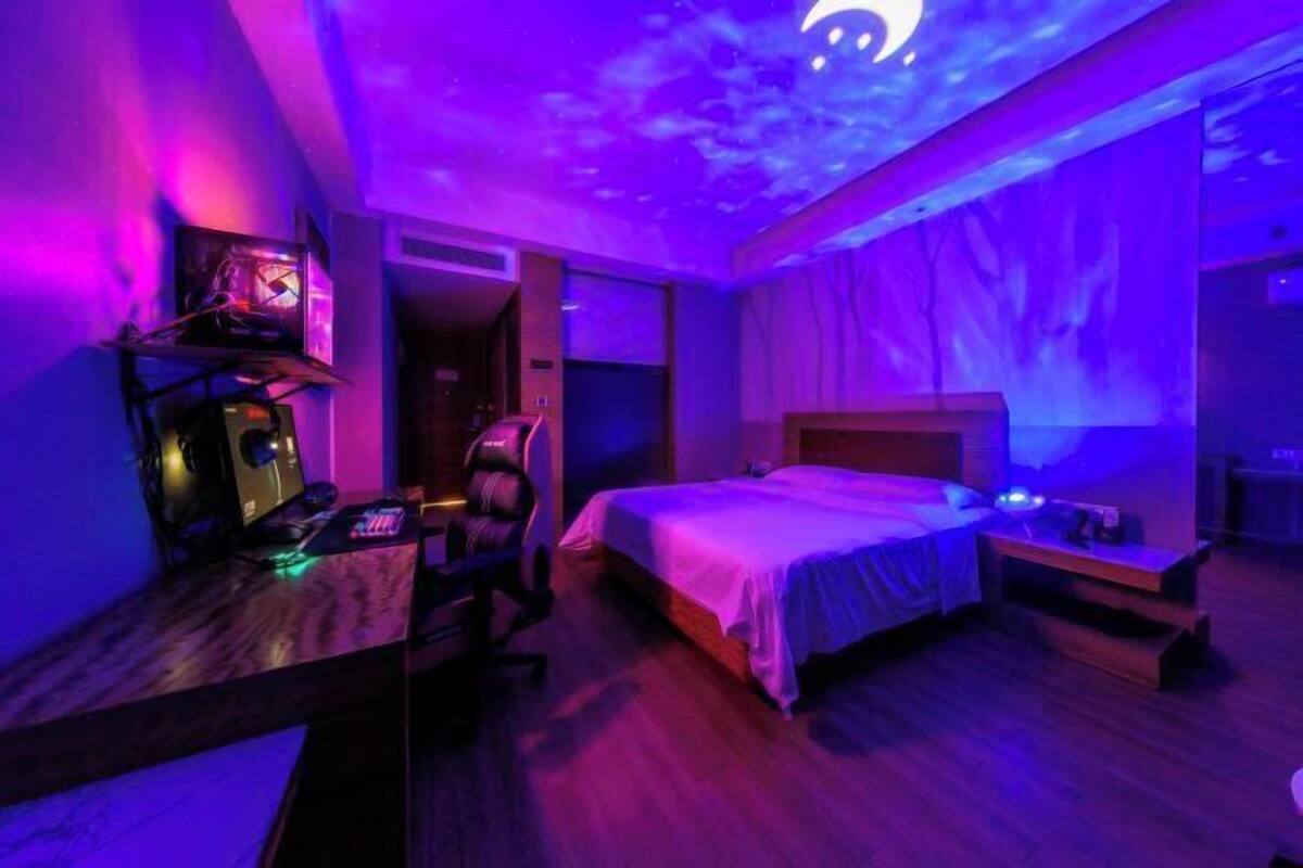 A bedroom with a bed, a desk with a computer, and a projector on the ceiling.