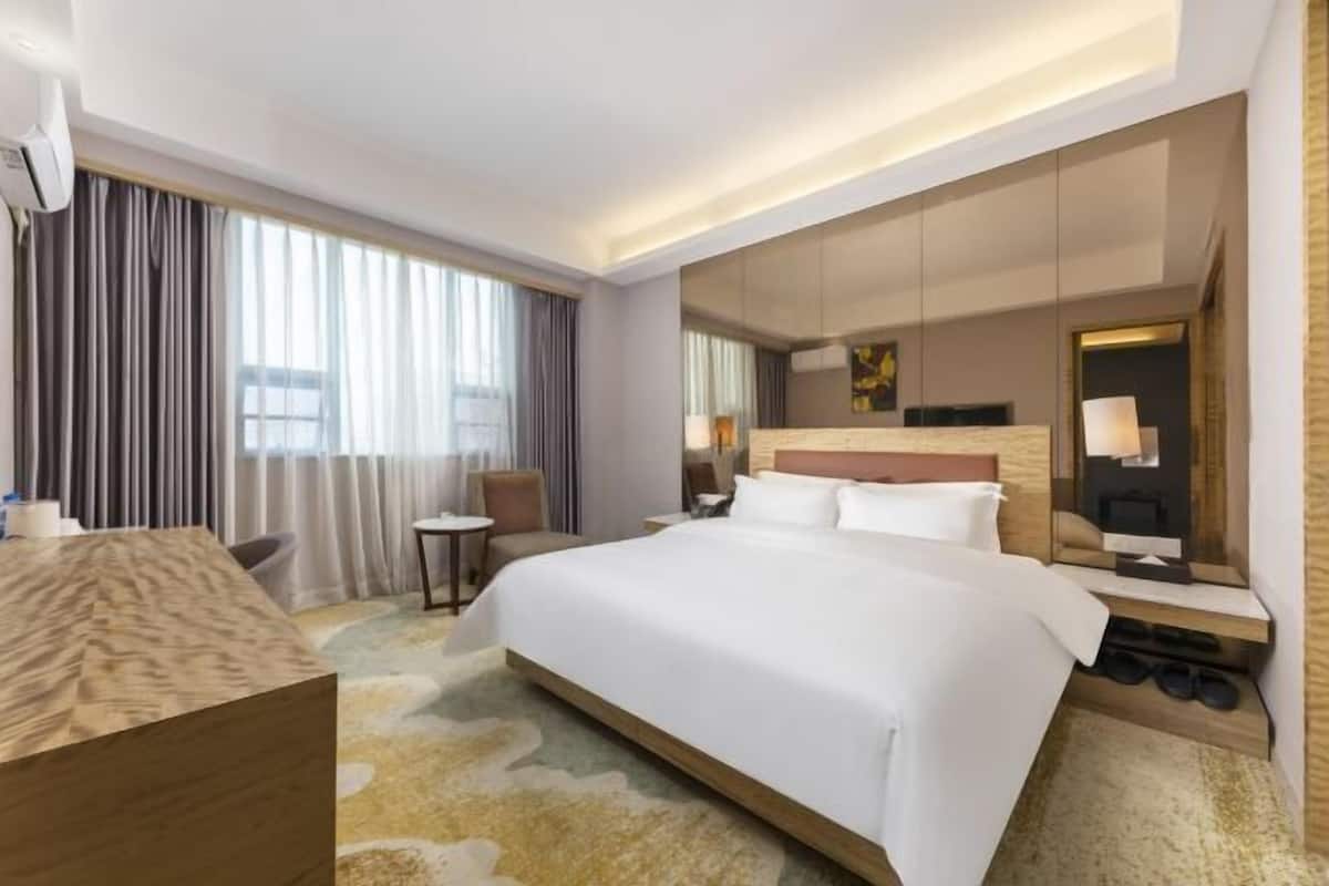 A hotel room with a large bed, a desk, a chair, a mirror, and a shoe rack.