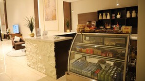 A hotel lobby with a reception desk, a seating area, a display case with snacks, and a wall-mounted television. - Afal Serviced Apartments - Al-Munsiyah (Riyadh)