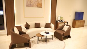 A modern living room with a sectional sofa, two armchairs, a coffee table, a television, and a decorative wall piece. - Afal Serviced Apartments - Al-Munsiyah (Riyadh)