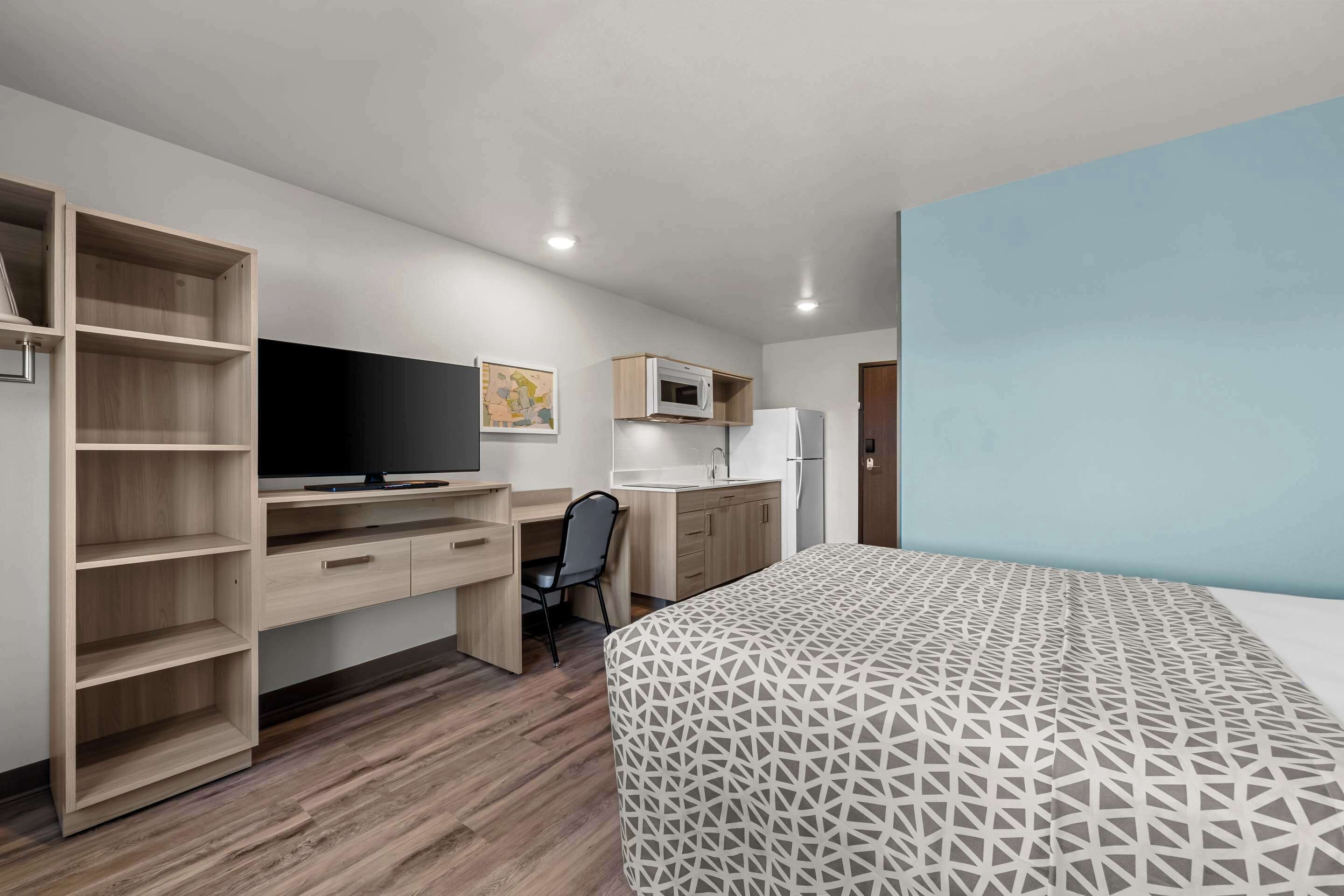 A bedroom with a bed, a desk with a chair, a wardrobe, a TV, a microwave, and a refrigerator.