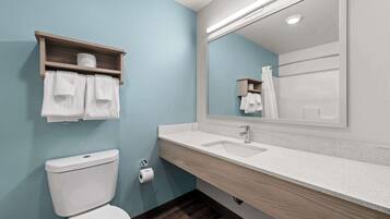 A bathroom with a toilet, a sink, a mirror, and a shelf with towels.