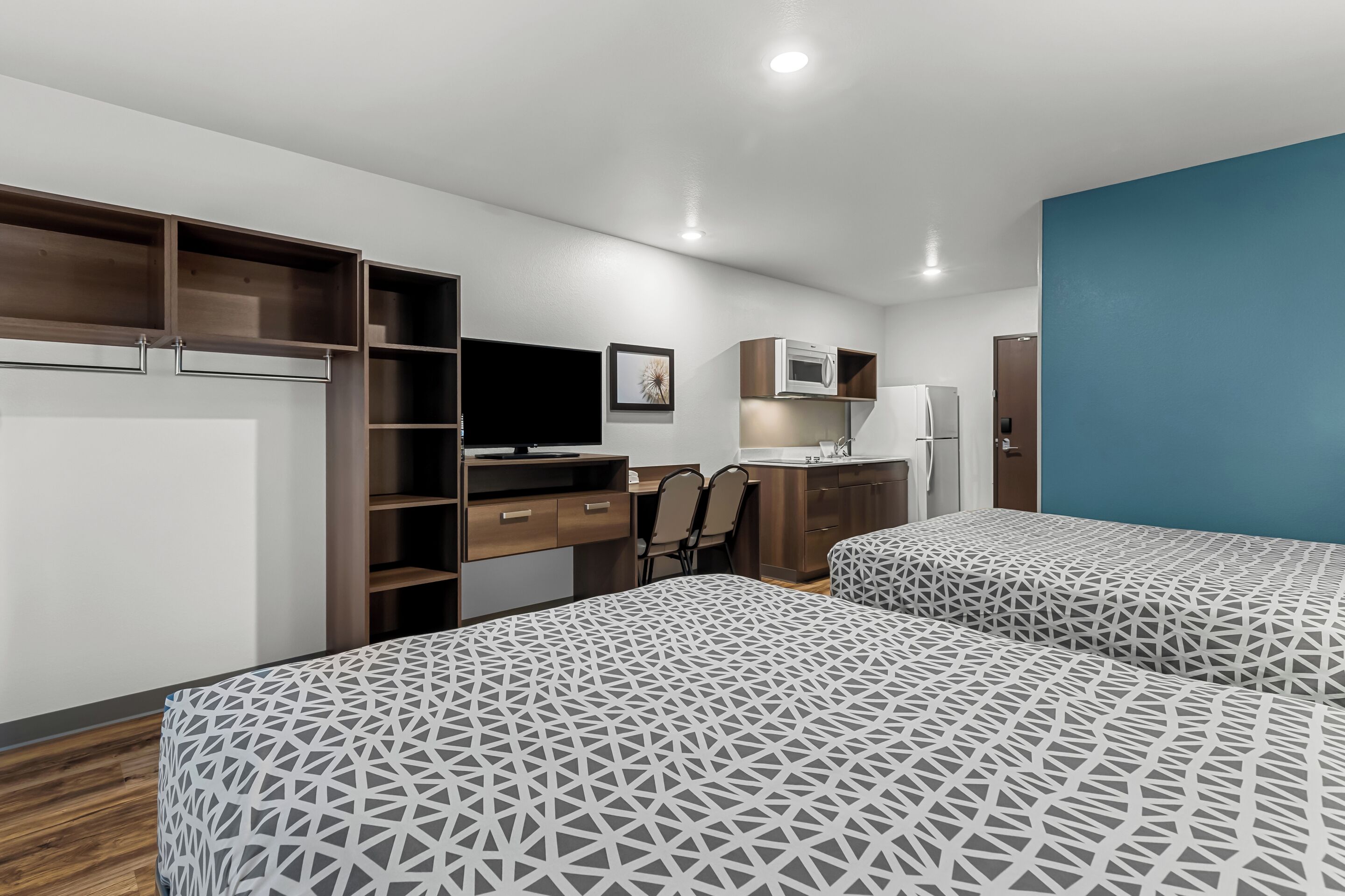 Una habitación de hotel moderna con dos camas, un escritorio, una silla, un televisor, un microondas y un refrigerador.