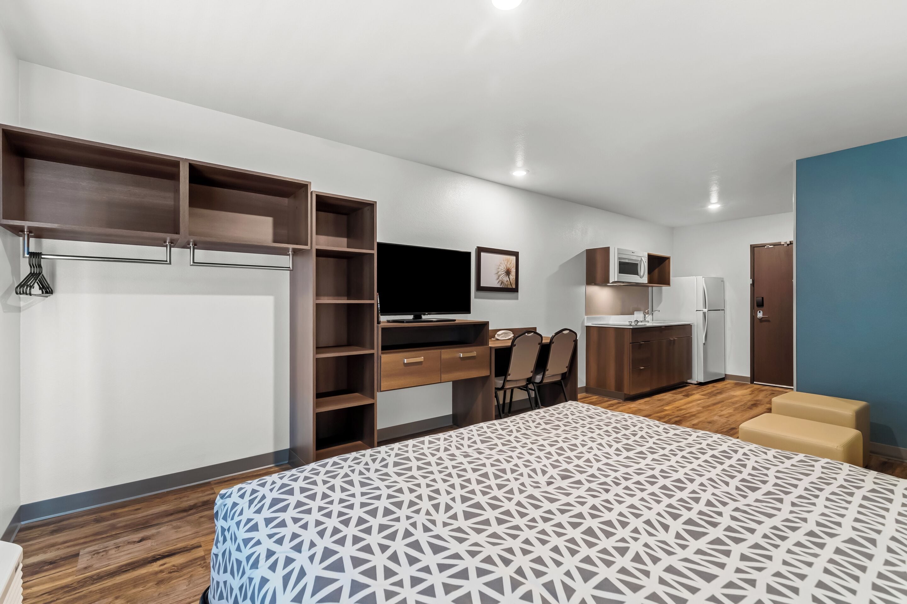 A modern bedroom with a large bed, built-in wardrobe, a desk, and a kitchenette.